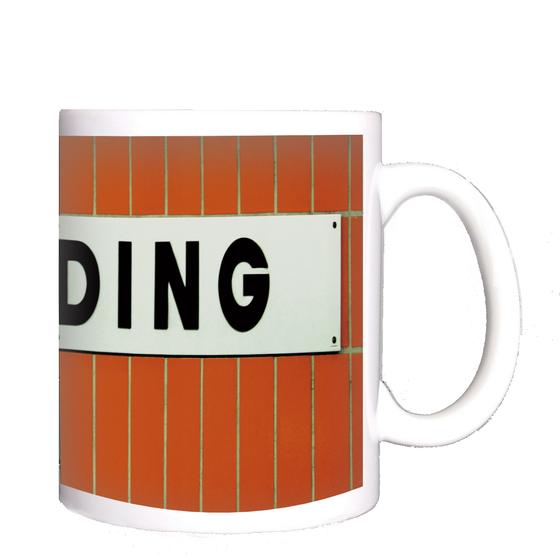 U-Bahnhof Wedding Kaffeetasse - weißes Schild mit schwarzer, schlichter Schrift auf orangen Fliesen