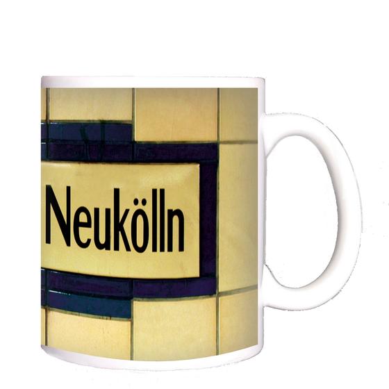 U-Bahnhof Rathaus Neukölln Kaffeetasse - schwarze Schrift auf gelblich-beigem Schild, umrandet von dunkelblauen Fliesen, welche wiederum von beigen Fliesen begrenzt werden