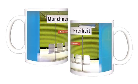 U-Bahnhof Münchner-Freiheit Kaffeetasse - weißes Schild mit schwarzer Schrift, im Hintergrund der Bahnhof mit zwei blauen Säulen, einer grasgrünen Wand in Jalousieoptik und fünf silbernen Bahnhofssitzen