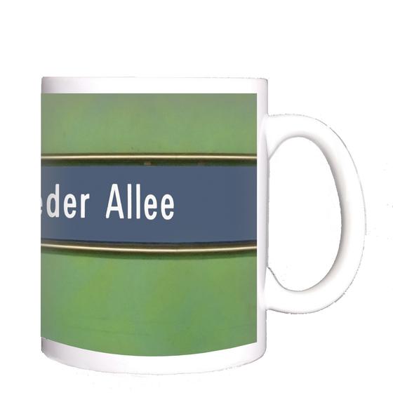 U-Bahnhof Forstenrieder Allee Kaffeetasse - weiße Schrift auf blauem Streifen, mit goldener Umrandung, vor grünem Hintergrund