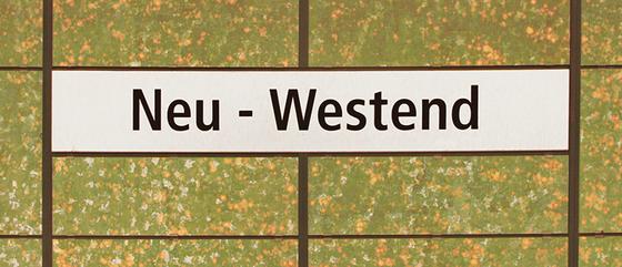 U-Bahnhof Neu-Westend Kaffeetasse - schwarze Schrift auf weißem Schild, vor grün-orange-weiß getupfter Wand