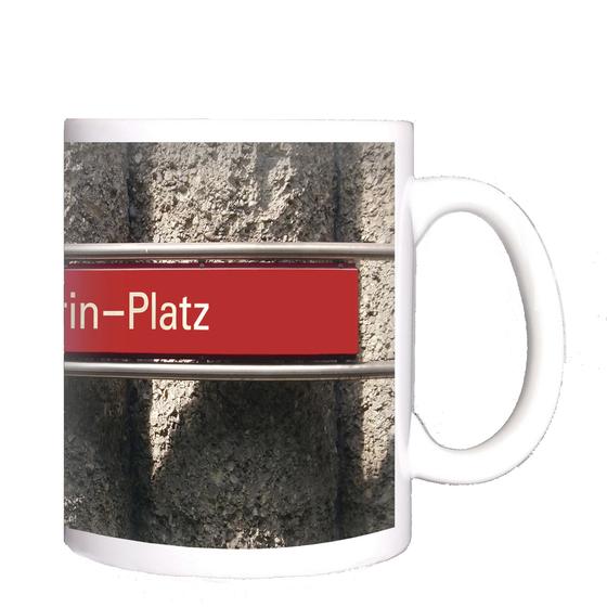 U-Bahnhof St.-Quirin-Platz Kaffeetasse - weiße Schrift auf blauem Schild, vor Betonsäulen-Wand