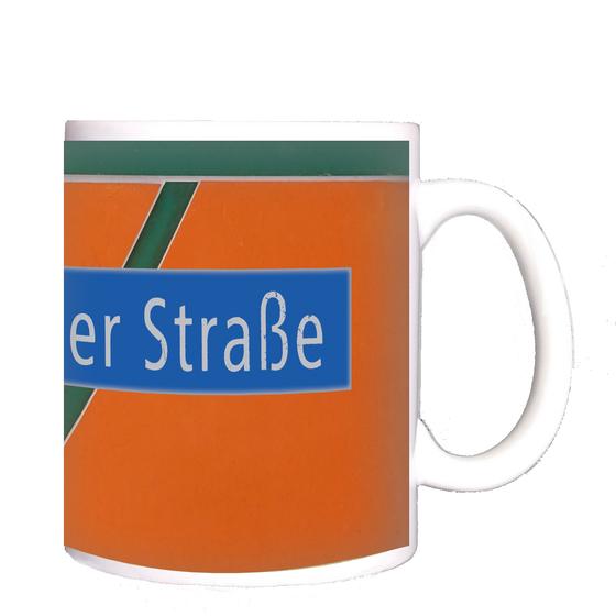 U-Bahnhof Holzhauser Straße Kaffeetasse - weiße Schrift auf blauem Schild vor orangem Hintergrund mit dunkelgrünem, diagonalem Streifen