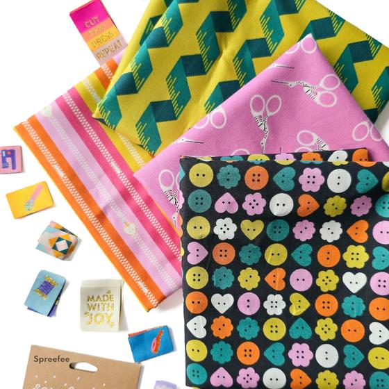 Bits and Bobs Stoffkollektion von Sarah Hearts für Figo Fabrics mit illustrierten Nähutensilien wie Scheren, Knöpfen und Maßbändern.