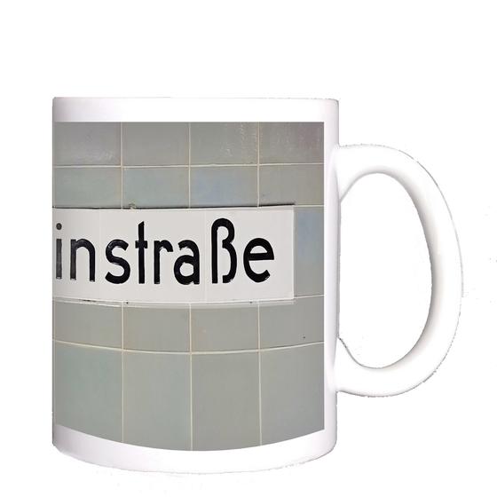 U-Bahnhof Schönleinstraße Kaffeetasse - schwarze Schrift auf weißem Schild vor fliederfarbenen quadratischen Kacheln