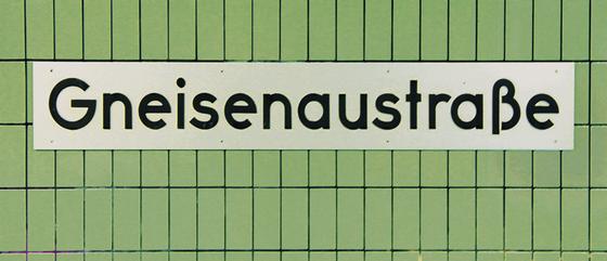 U-Bahnhof Gneisenaustraße Kaffeebecher - weißes Schild mit schwarzer Schrift, vor grüner Fliesenwand.