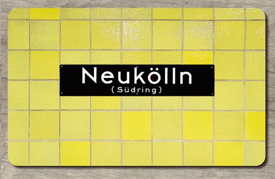 U-Bahnhof Neukölln Frühstücksbrettchen - schwarzes Schild mit weißer Schrift auf gelbem Fliesenhintergrund
