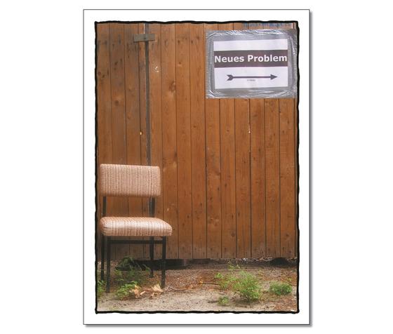 Klassische Postkarte - Abbildung eines Stuhles vor einer Holzwand mit angeklebten Schild mit der Aufschrift "Neues Problem" und einem Pfeil nach rechts. 
