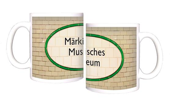 U-Bahnhof Märkisches Museum Kaffeetasse - schwarze Schrift auf ovalem, weißem Schild aus Fliesen, mit grüner Umrandung, vor hellbeigen Kacheln