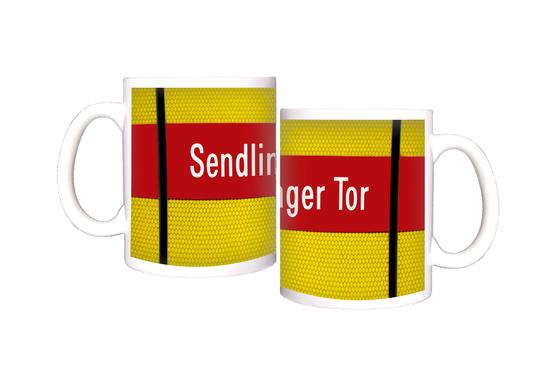 U-Bahnhof Sendlinger Tor Kaffeetasse - weiße Schrift auf rotem Streifen, vor gelbem Raster, durchzogen von schwarzem Senkrechtstreifen