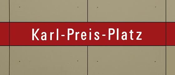 U-Bahnhof Karl-Preis-Platz Kaffeetasse - weiße Schrift auf dunkelrotem Streifen, vor grau-brauner Plattenwand