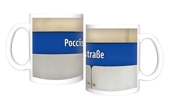 U-Bahnhof Poccistraße Kaffeetasse - weiße Schrift auf dunkelblauem Streifen, vor weißer Plattenwand