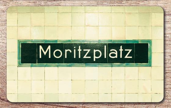 U-Bahnhof Moritzplatz Frühstücksbrettchen - schwarzes Schild mit grünem Rand und weißer Schrift auf beigem Fliesenhintergrund