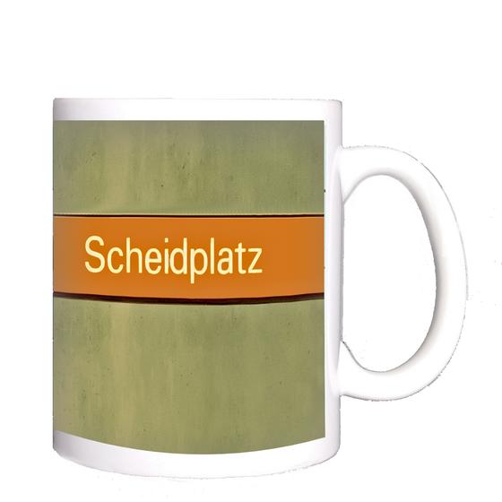 U-Bahnhof Scheidplatz Kaffeetasse - weiße Schrift auf orangem Streifen, vor braun-beiger Wand mit blauen Fliesen am linken Rand