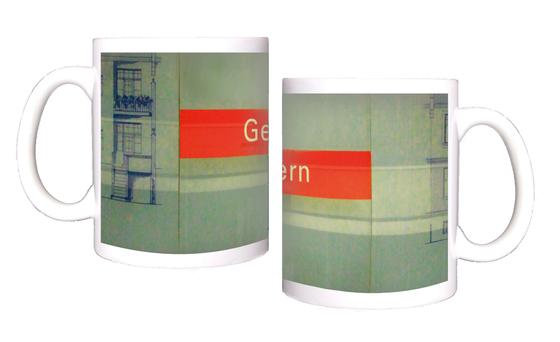 U-Bahnhof Gern Kaffeetasse - weiße Schrift auf rotem Schild, vor grauer Steinwand, mit blauer Zeichnung auf der linken Seite