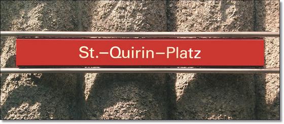 U-Bahnhof St.-Quirin-Platz Kaffeetasse - weiße Schrift auf blauem Schild, vor Betonsäulen-Wand