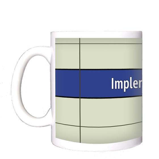 U-Bahnhof Implerstraße Kaffeetasse - weiße Schrift auf blauem Streifen, vor weißem Plattenhintergrund