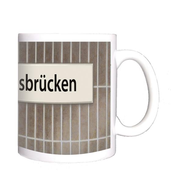 U-Bahnhof Landungsbrücken Kaffeetasse - schwarze Schrift auf weißem Schild vor braun-grauer Fliesenwand