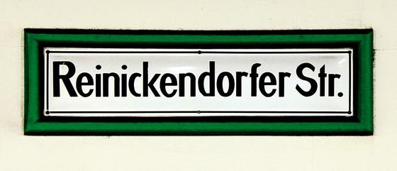 U-Bahnhof Reinickendorfer Straße Kaffeetasse - schwarze Schrift auf weißem Schild, mit dickem, grünem Rahmen, vor weißer Wand