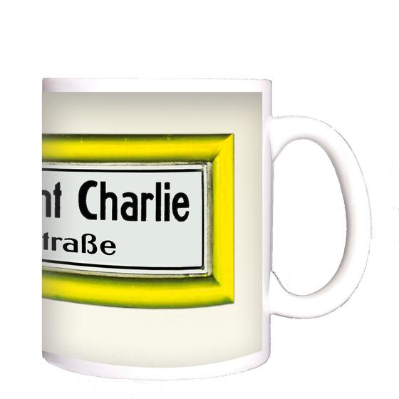 U-Bahnhof Checkpoint Charlie Kochstrasse Kaffeetasse - schwarze Schrift auf weißem Schild mit gelbem Rahmen, vor weisser Wand