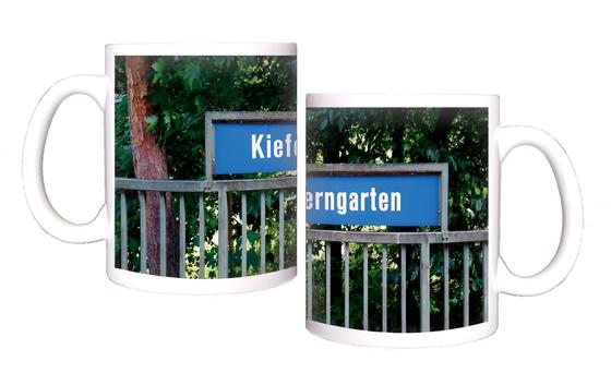 U-Bahnhof Kieferngarten Kaffeetasse - weiße Schrift auf blauem Schild, über Metallzaun, vor Bäumen