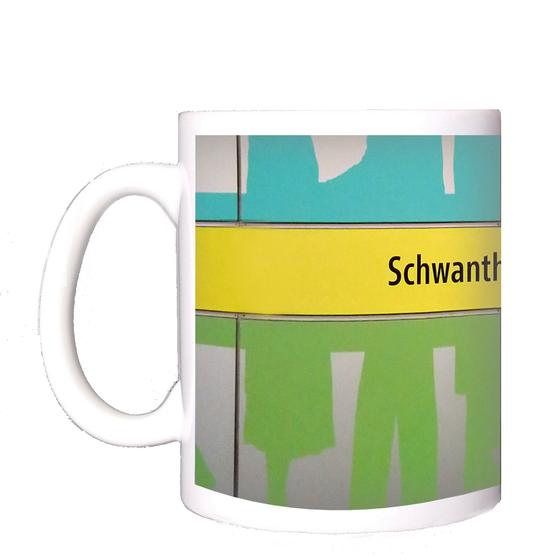 U-Bahnhof Schwanthalerhöhe Kaffeetasse - schwarze Schrift auf gelbem Streifen, zwischen grünem und blauem Querstreifen mit abstrakten Mustern