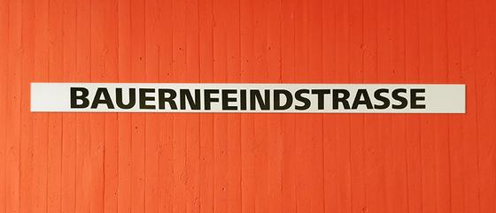U-Bahn-Tasse Nuernberg Bauernfeindstrasse der Linie U1 in der originalgetreuen Stations-Gestaltung - schwarze Schrift auf weißem Streifen, oranger Streifenbeton Hintergrund 