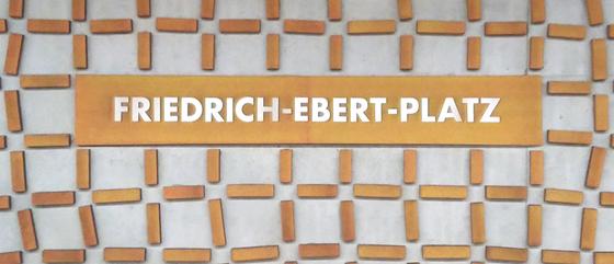 U-Bahn-Tasse Nuernberg Friedrich-Ebert-Platz der Linie U3 in der originalgetreuen Stations-Gestaltung - Hellblaugraue Wand mit rostig orangener Netzstruktur, Schild in gleicher Farbe mit weisser Schrift