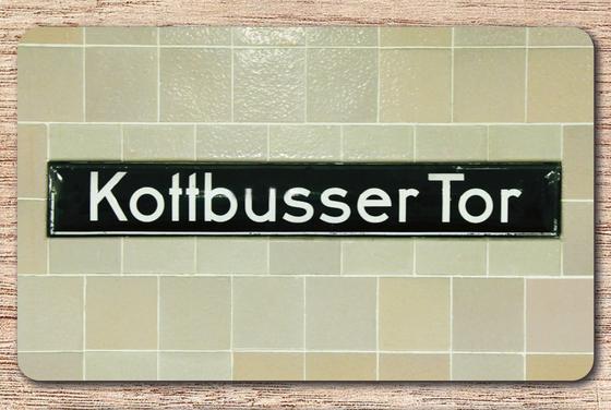 U-Bahnhof Kottbusser Tor Frühstücksbrettchen - schwarzes Schild mit weißer Schrift auf gräulichem Pastell-Fliesenhintergrund