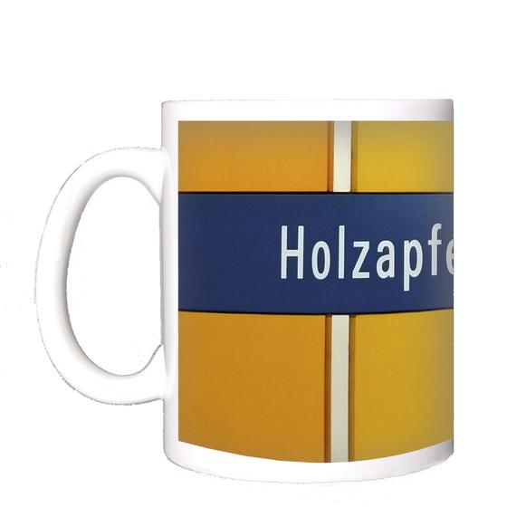 U-Bahn-Tasse mit dem Schriftzug des Muenchner Bahnhofs Holzapfelkreuth der Linie U6 - Dunkelblaues Schild mit weissem Text auf orangenem Grund  