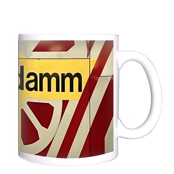 U-Bahn-Kaffeetasse Berlin Rohrdamm - schwarze Schrift auf gelbem Schild, umrandet von weißem, radähnlichem Muster auf rot-braunem Untergrund