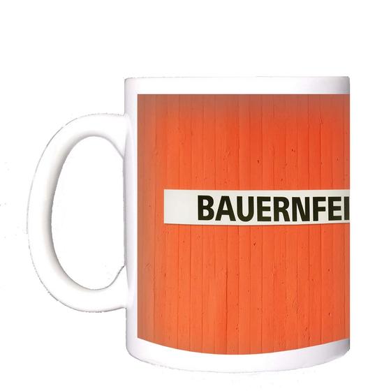 U-Bahn-Tasse Nuernberg Bauernfeindstrasse der Linie U1 in der originalgetreuen Stations-Gestaltung - schwarze Schrift auf weißem Streifen, oranger Streifenbeton Hintergrund 