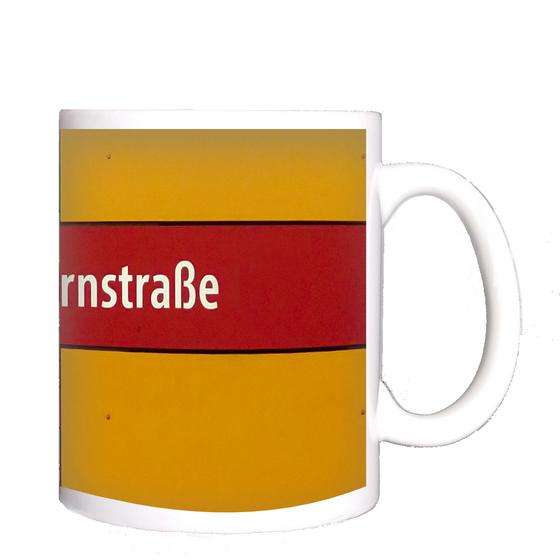 U-Bahnhof Silberhornstraße Kaffeetasse - weiße Schrift auf rotem Streifen, vor dunkelgelbem Hintergrund