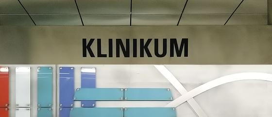 U-Bahn-Tasse Fuerth Klinikum der Nuernberger Linie U1 in der originalgetreuen Stations-Gestaltung - grau-beiges Schild mit schwarzer Schrift, an der Rückwand farbige, brettartige Panelen als Gestaltungselemente