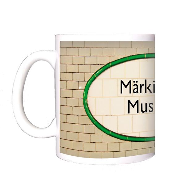 U-Bahnhof Märkisches Museum Kaffeetasse - schwarze Schrift auf ovalem, weißem Schild aus Fliesen, mit grüner Umrandung, vor hellbeigen Kacheln