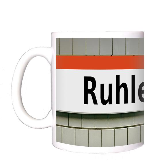 U-Bahnhof Ruhleben Kaffeetasse - schwarze Schrift auf weißem Schild mit orangem Streifen auf weißer Fliesenwand