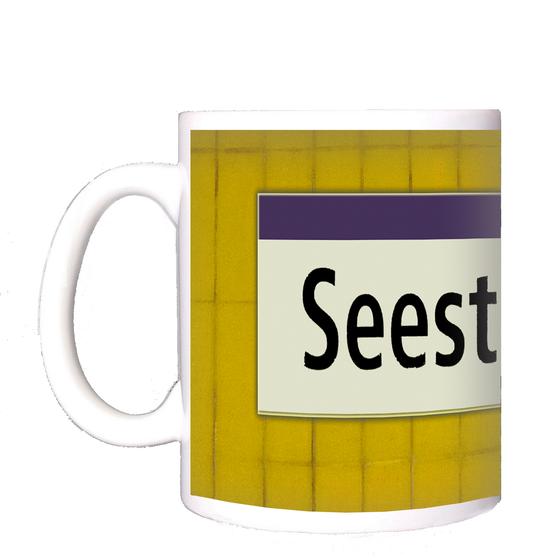 U-Bahnhof Seestraße Kaffeetasse - schwarze Schrift auf weißem Schild mit lila Streifen, vor gelber Mosaikwand