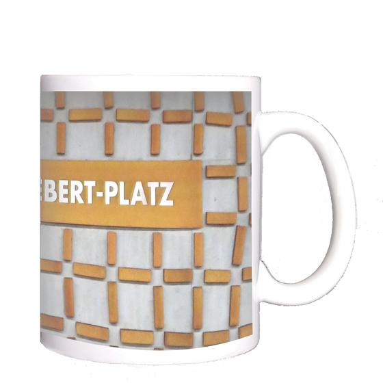 U-Bahn-Tasse Nuernberg Friedrich-Ebert-Platz der Linie U3 in der originalgetreuen Stations-Gestaltung - Hellblaugraue Wand mit rostig orangener Netzstruktur, Schild in gleicher Farbe mit weisser Schrift