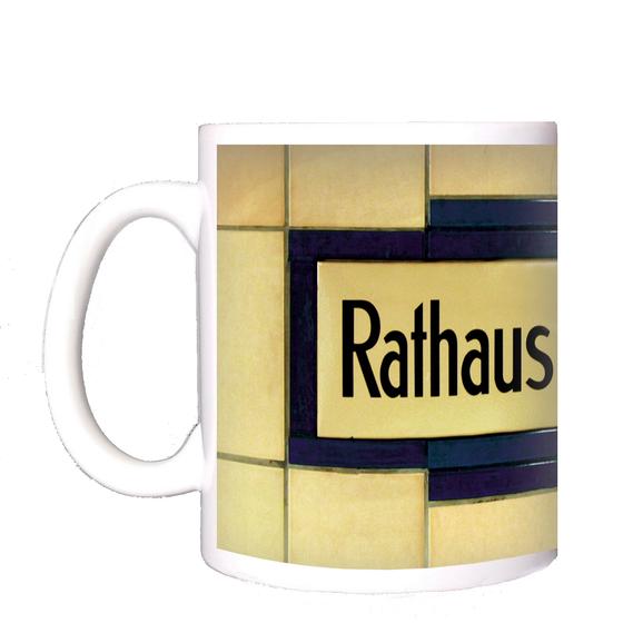 U-Bahnhof Rathaus Neukölln Kaffeetasse - schwarze Schrift auf gelblich-beigem Schild, umrandet von dunkelblauen Fliesen, welche wiederum von beigen Fliesen begrenzt werden