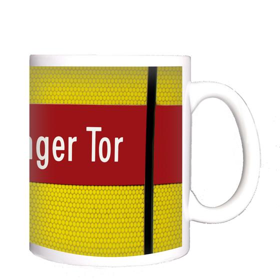 U-Bahnhof Sendlinger Tor Kaffeetasse - weiße Schrift auf rotem Streifen, vor gelbem Raster, durchzogen von schwarzem Senkrechtstreifen