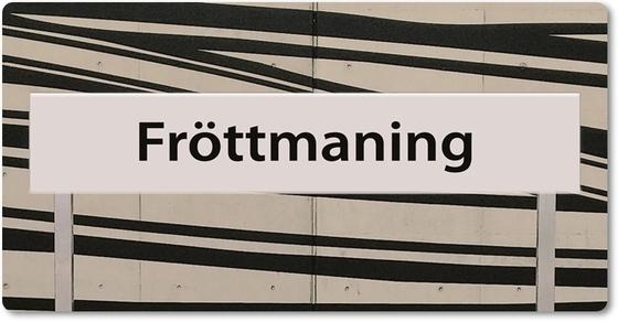 U-Bahnhof Fröttmaning Kühlschrankmagnet - schwarze Schrift auf weißem Schild, vor weißem Hintergrund mit dynamischen, schwarzen Streifen