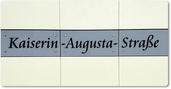 U-Bahnhof Kaiserin-Augusta-Straße - Schwarze, geschwungene Schrift auf grau-blauem Schild vor weißem Fliesenhintergrund