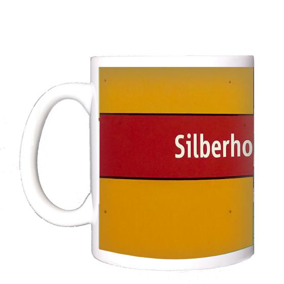 U-Bahnhof Silberhornstraße Kaffeetasse - weiße Schrift auf rotem Streifen, vor dunkelgelbem Hintergrund