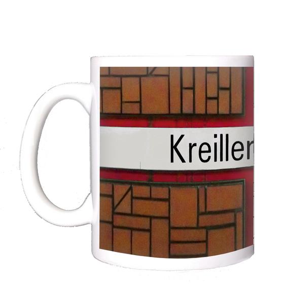 U-Bahnhof Kreillerstraße Kaffeetasse - schwarze Schrift auf weißem Schild, welches Teil eines roten Kreuzes ist, vor zweigeteiltem Hintergrund mit schwarz-weißen Punkten und rot-braunem Backsteinmuster