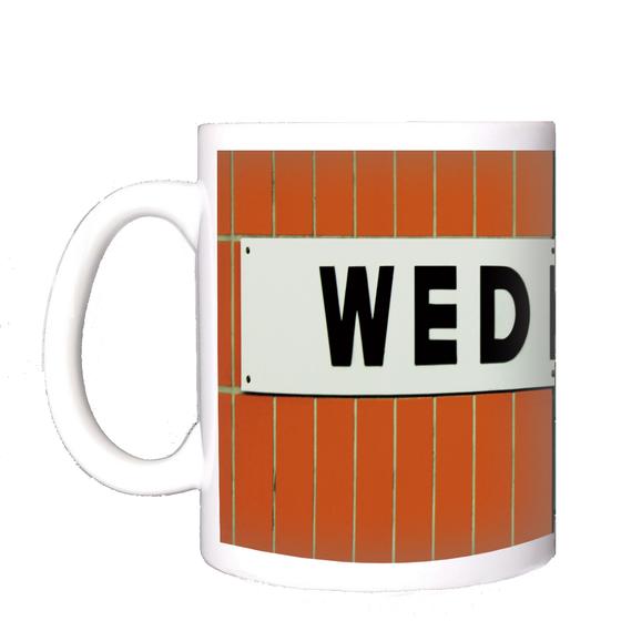 U-Bahnhof Wedding Kaffeetasse - weißes Schild mit schwarzer, schlichter Schrift auf orangen Fliesen