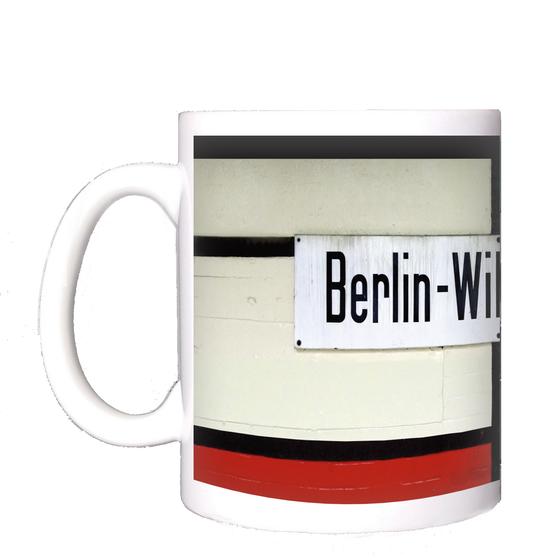 Kaffeebecher mit Aufdruck der originalgetreuen Gestaltung des Berliner S-Bahnhofs Wilhelmsruh rund um das Stationsschild - weiss gestrichene Ziegel mit balkenartigen schwarzen Verstrebungen, die ein weisses Emailleschild mit schwarzer Schrift einrahmen - 