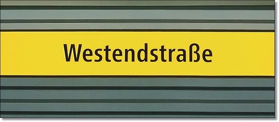 U-Bahnhof Westendstraße Kaffeetasse - schwarzer Schrift auf gelbem Schild, vor grau-blauer Wand mit schwarzen Streifen