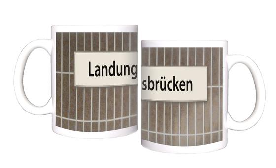 U-Bahnhof Landungsbrücken Kaffeetasse - schwarze Schrift auf weißem Schild vor braun-grauer Fliesenwand