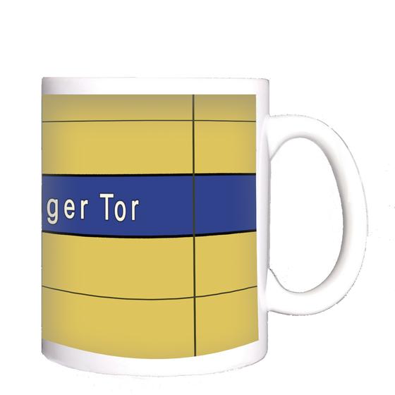 U-Bahnhof Sendlinger Tor Kaffeetasse - weiße Schrift auf blauem Streifen, vor gelber Plattenwand