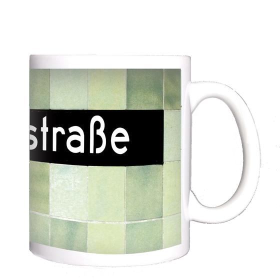 U-Bahnhof Voltastrasse Kaffeetasse - weiße Schrift auf schwarzem Schild, vor Mosaikwand in diversen Grüntönen
